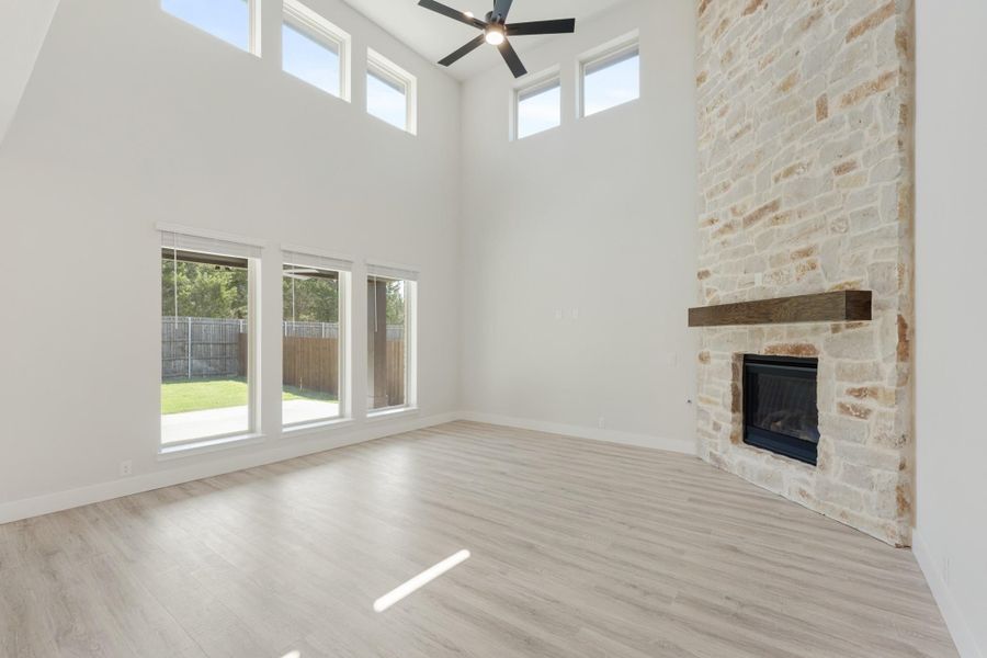 Open living room with two-story ceiling, stone fireplace, ceiling fan, and light wood floors