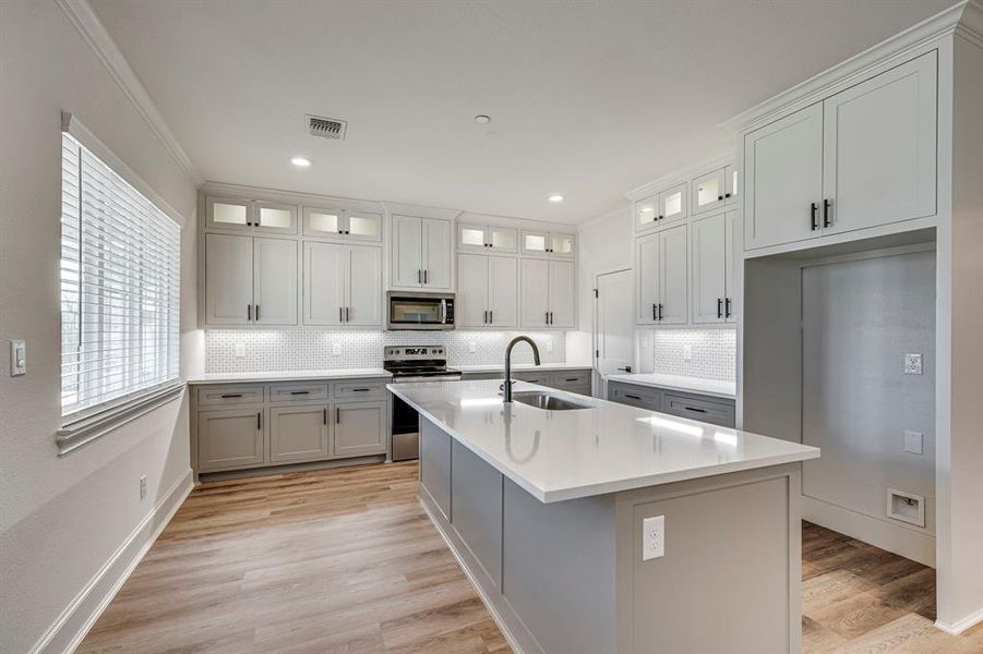 Kitchen featuring backsplash, a sink, stainless steel appliances, visible vents, and light wood-style floors Kitchen featuring backsplash, a sink, stainless steel appliances, visible vents, and light wood-style floors