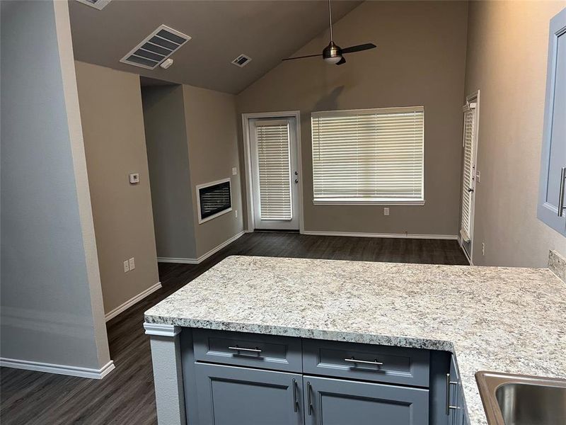 Kitchen with dark wood-type flooring, ceiling fan, baseboards, high vaulted ceiling, and a peninsula