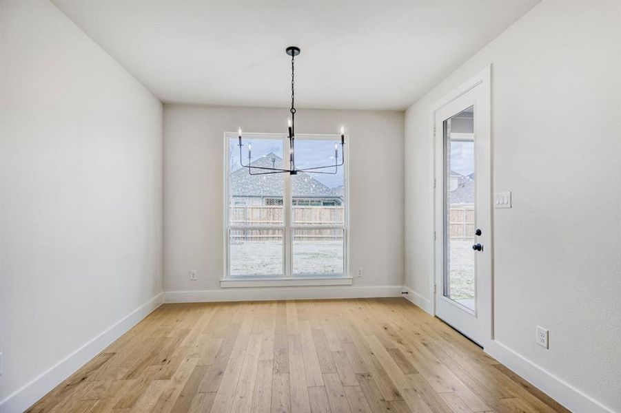 Spacious room featuring wood-finish flooring, a contemporary black chandelier, and a large window providing ample natural light