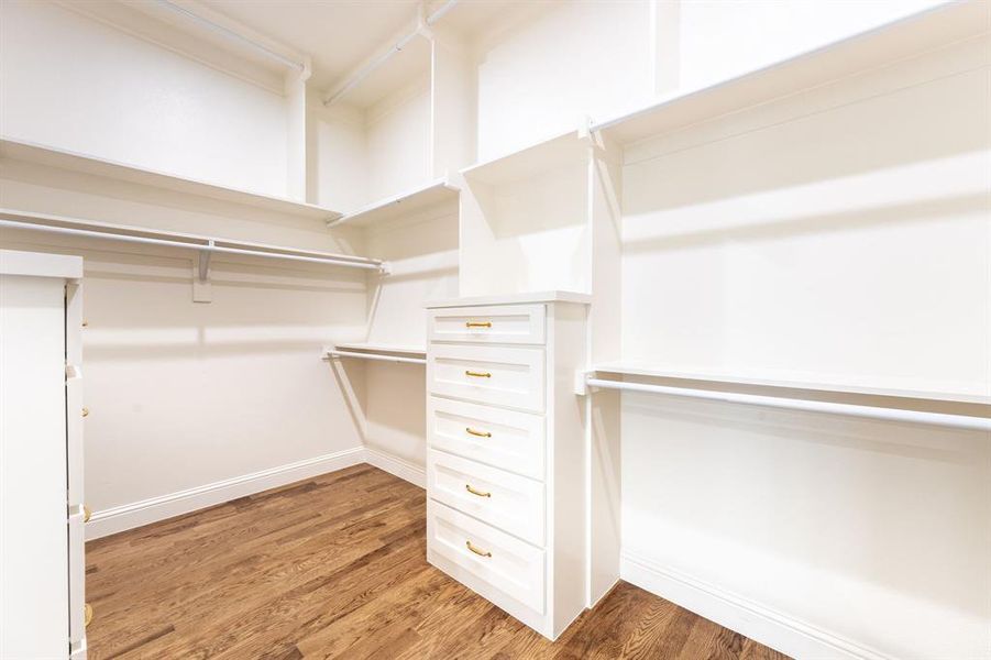 Walk-in closet featuring built-in cabinetry, multiple shelving units, hanging rods, and wood-finish flooring Walk-in closet featuring built-in cabinetry, multiple shelving units, hanging rods, and wood-finish flooring
