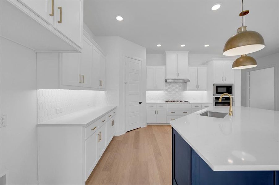Dual tone kitchen featuring light wood-style flooring, light stone counters, a kitchen island with sink, dual tone cabinets, and pendant lighting
