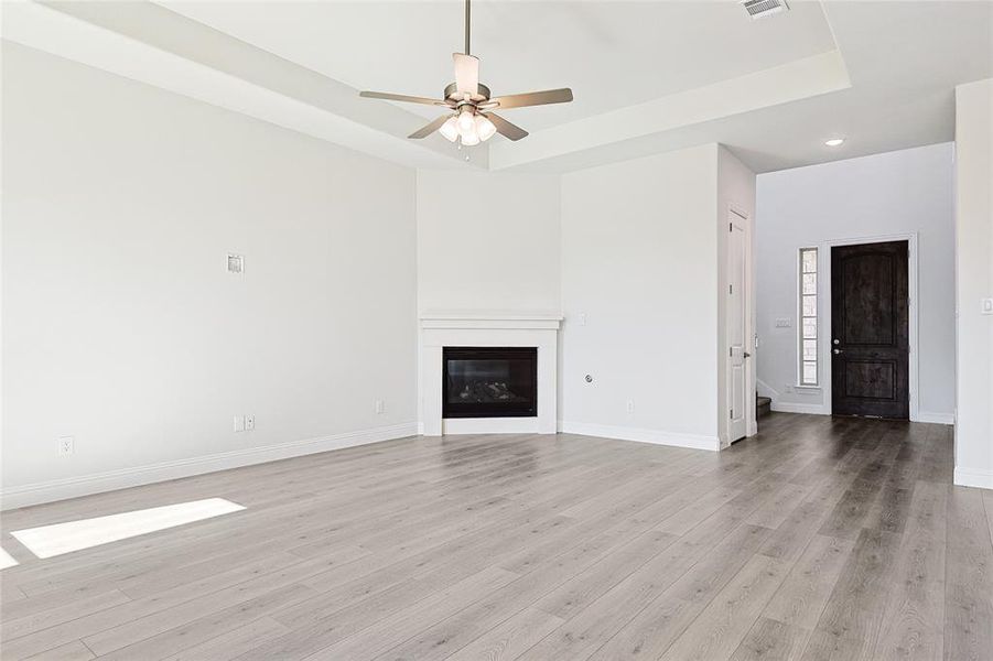 Unfurnished living room featuring light hardwood / wood-style floors, a raised ceiling, and ceiling fan