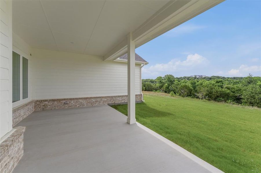 Covered patio with a concrete surface, featuring a white horizontal siding exterior with a brick foundation accent Covered patio with a concrete surface, featuring a white horizontal siding exterior with a brick foundation accent