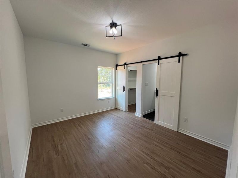 Master bedroom with a barn door and hardwood / wood-style floors