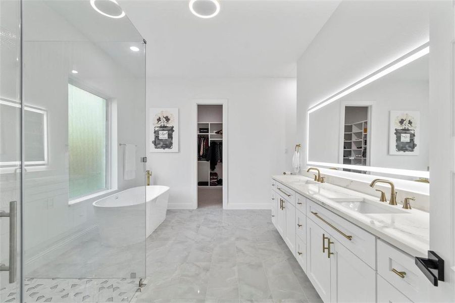 Bathroom featuring a walk in closet, double vanity, a stall shower, a freestanding tub, and recessed lighting