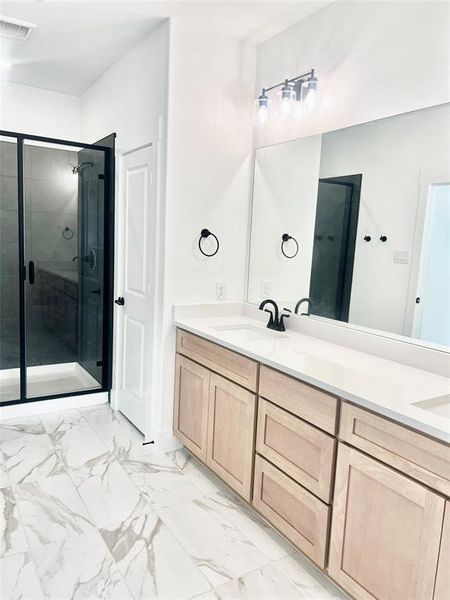 Bathroom featuring a stall shower, double vanity, and light marble finish flooring
