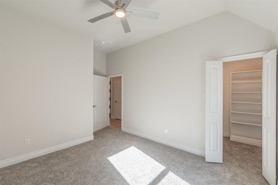 Unfurnished bedroom featuring light carpet, ceiling fan, a spacious closet, a closet, and lofted ceiling