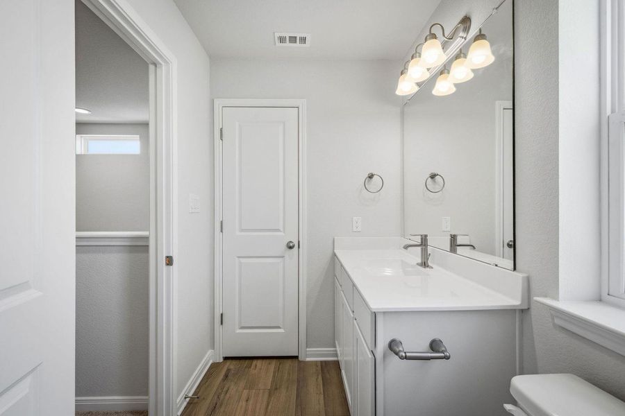 Rich wood-textured flooring contrasts beautifully with a clean white vanity and classic glass block windows. Rich wood-textured flooring contrasts beautifully with a clean white vanity and classic glass block windows.