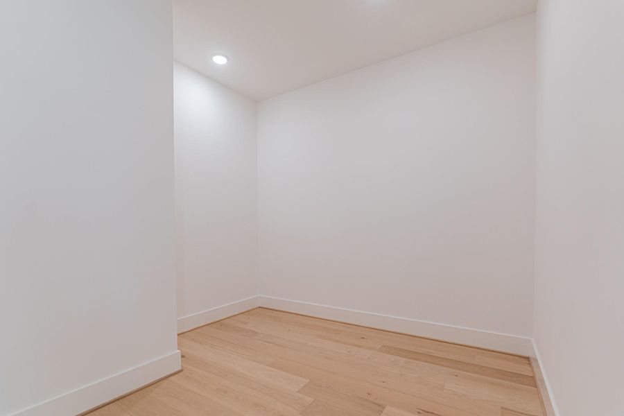This photo showcases a small, unfurnished room with white walls and light wood flooring. It has recessed lighting, giving it a clean and modern feel, ideal for use as a storage space or a cozy nook.