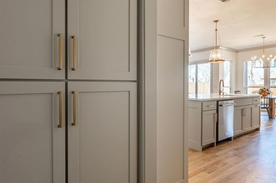 Kitchen with light wood-style flooring, suspended lighting, gray cabinetry, stainless steel dishwasher, and light stone counters
