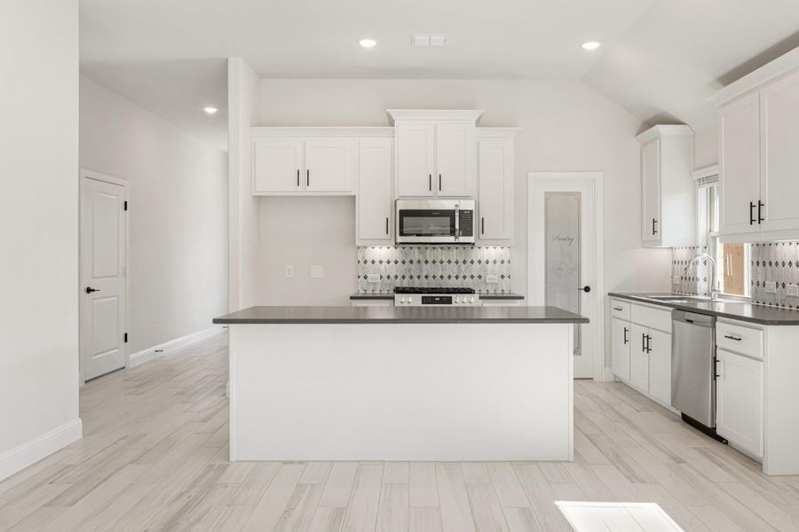 White kitchen with center island, dark countertops, stainless steel appliances, and patterned tile backsplash