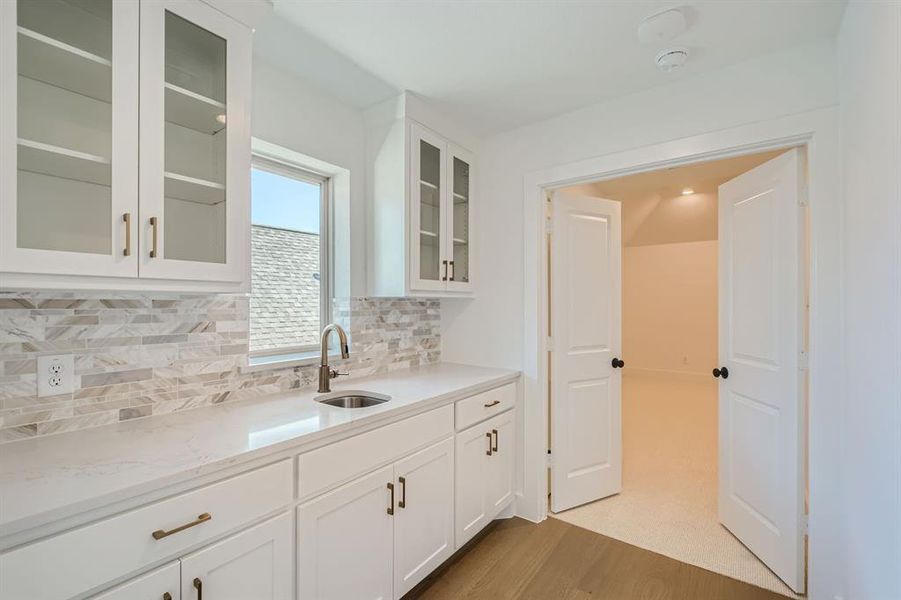 Kitchen featuring light stone counters, light hardwood / wood-style floors, tasteful backsplash, sink, and white cabinets