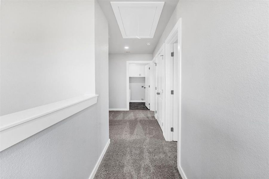 Hallway with attic access, carpet, and baseboards