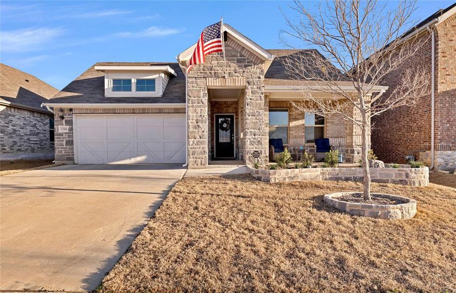 View of front of property with stone siding, driveway, a garage, and roof with shingles