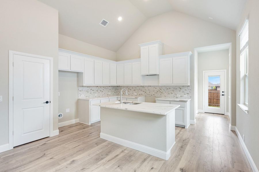 Kitchen with white cabinets, center island with sink, tile backsplash, and vaulted ceiling over light wood floors