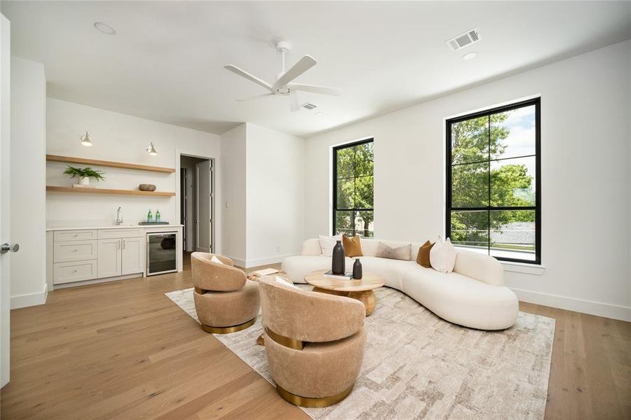 Living area with beverage cooler, bar with sink, light wood-style flooring, and ceiling fan