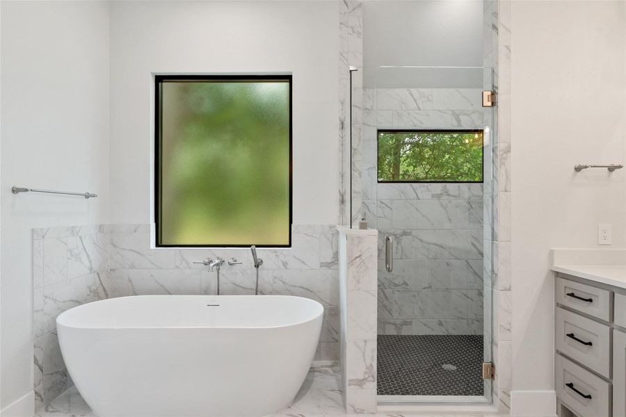 Marble-clad bathroom with a freestanding tub and a glass-enclosed shower, offering serene views.