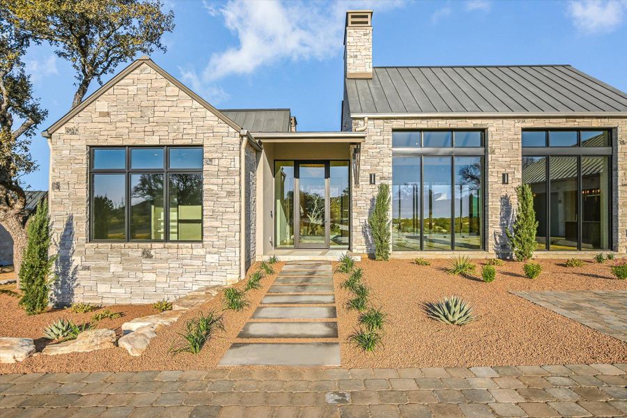 Back of house with stone siding, a chimney, and a standing seam roof