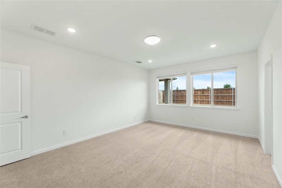 Empty bedroom with beige carpet, white walls, recessed lighting, and a window overlooking a wood fence