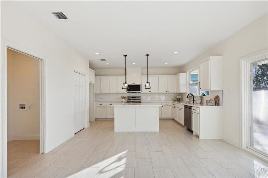 Kitchen with white cabinetry, tasteful backsplash, decorative light fixtures, a center island, and appliances with stainless steel finishes