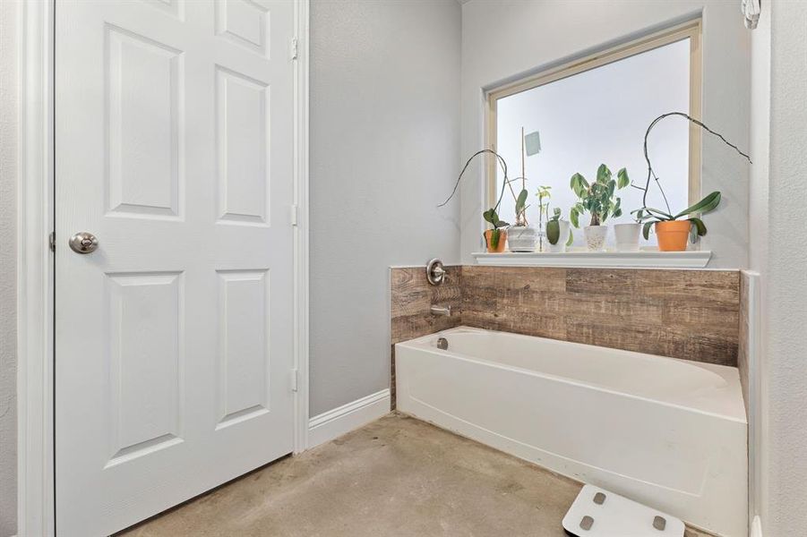 Bathroom with concrete flooring and a tub to relax in