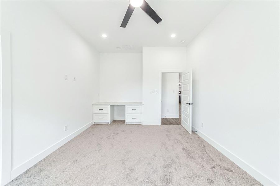 Unfurnished bedroom with light colored carpet, ceiling fan, built in desk, and recessed lighting