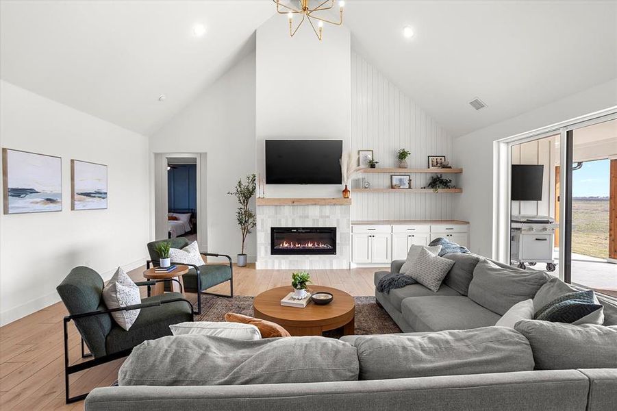 Living room with a notable chandelier, light hardwood / wood-style floors, high vaulted ceiling, and a tiled fireplace