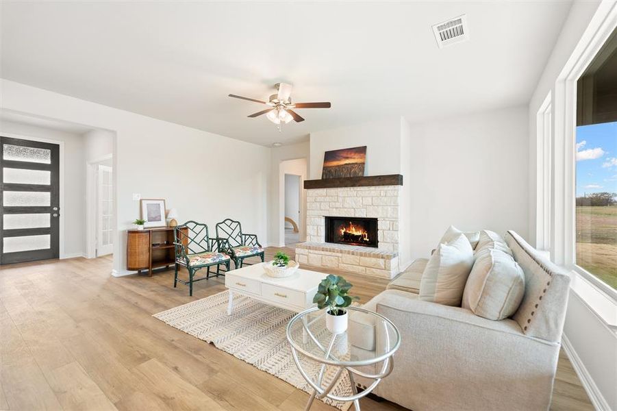 Living room with light wood-style flooring, a stone fireplace, and a ceiling fan