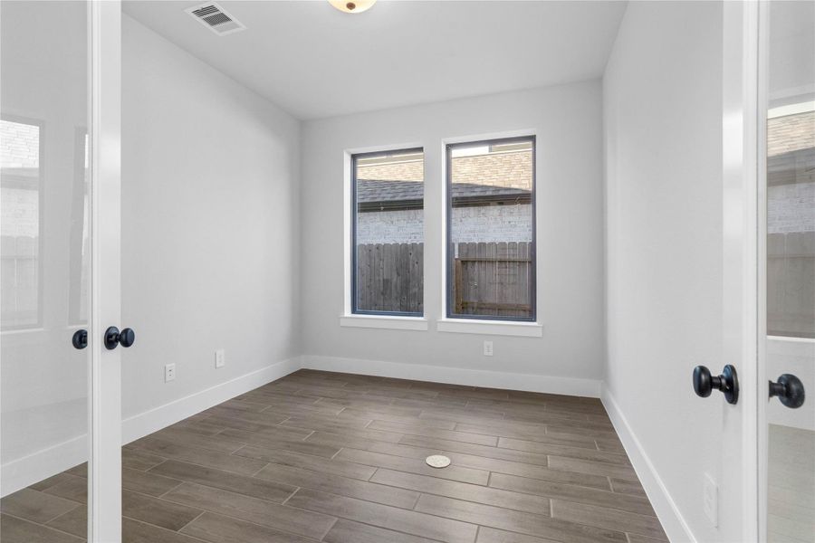 This handsome home office features wood-look tile flooring, large windows, high ceilings, recessed lighting, and custom paint!