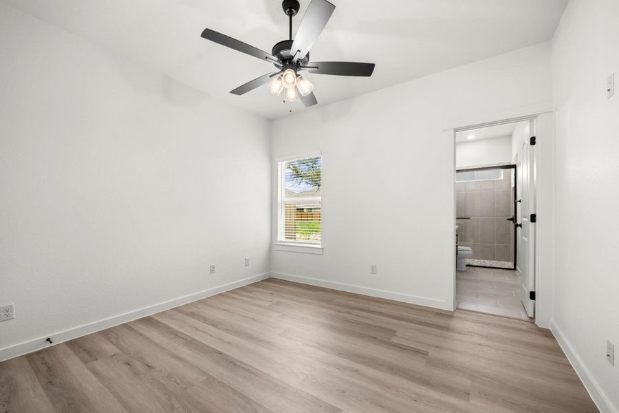A well-lit bedroom features durable laminate flooring and a direct view into the adjacent bath. A well-lit bedroom features durable laminate flooring and a direct view into the adjacent bath.