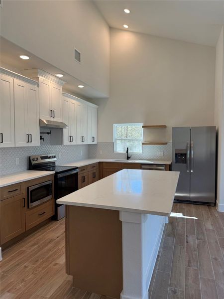 Kitchen with stainless steel appliances, light wood-style floors, a kitchen island, white cabinetry, and a high ceiling