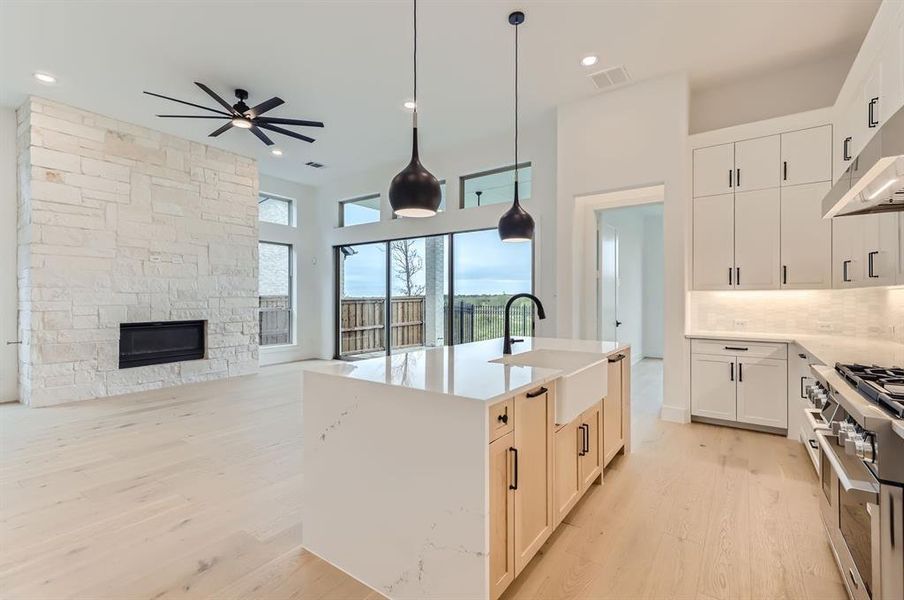 Kitchen featuring ceiling fan, an island with sink, hanging light fixtures, sink, and a fireplace