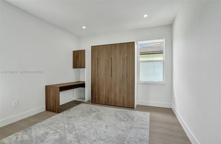 Recessed ceiling lighting, wood look flooring, built-in desk with overhead cabinetry