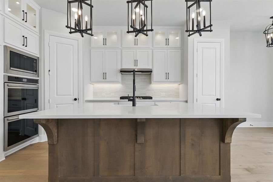 Kitchen featuring glass insert cabinets, hanging light fixtures, and white cabinets