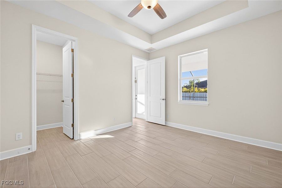 Unfurnished bedroom featuring a spacious closet, a raised ceiling, wood tiled floors, and a ceiling fan