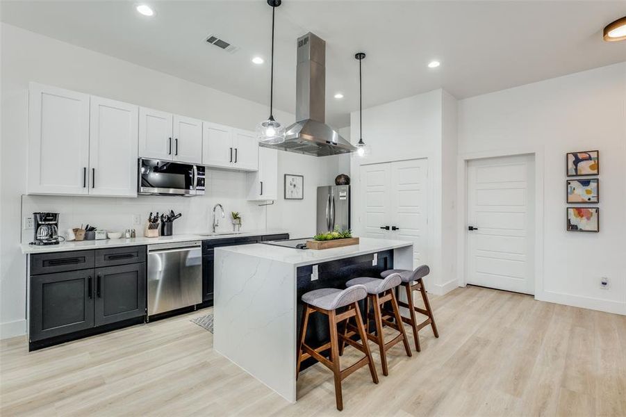 Kitchen with stainless steel appliances, island exhaust hood, light hardwood / wood-style floors, and pendant lighting