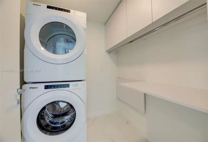 Laundry area featuring stacked white washer and dryer, white cabinetry, integrated shelving, and white tile flooring
