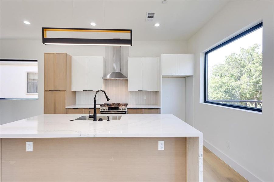 Kitchen featuring light stone counters, an island with sink, white cabinets, decorative backsplash, and wall chimney range hood