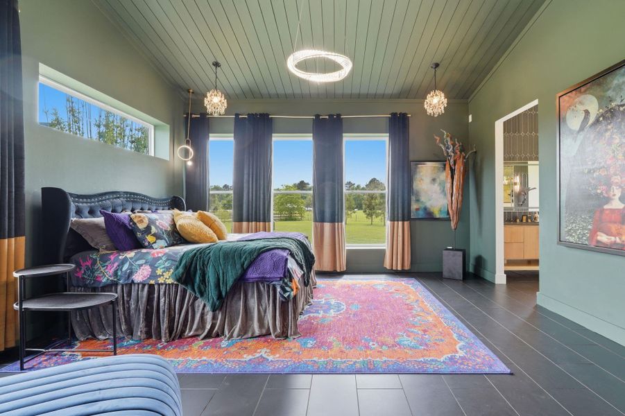 This spacious bedroom features a modern design with green walls and ceiling, large windows offering scenic views, and stylish lighting fixtures. It includes a plush bed with colorful bedding, a vibrant area rug, and tasteful decor, creating a cozy and inviting atmosphere.