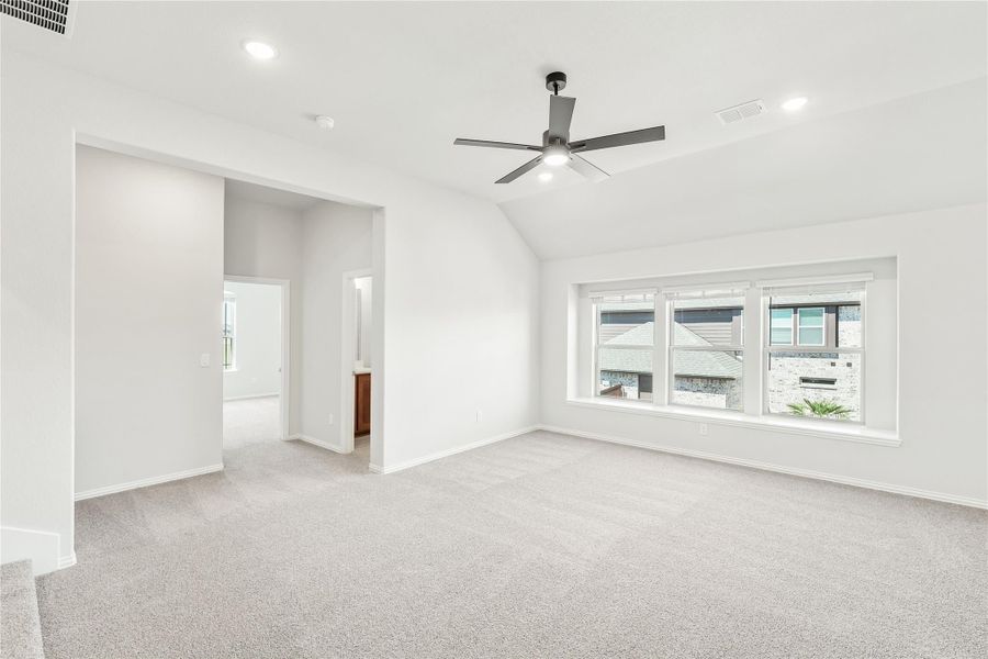 Spacious empty bedroom with vaulted ceiling, ceiling fan, carpet flooring, and large windows