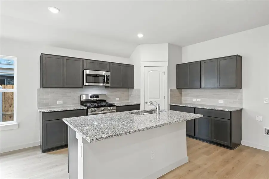 Kitchen with appliances with stainless steel finishes, light stone countertops, light wood-style floors, tasteful backsplash, and recessed lighting