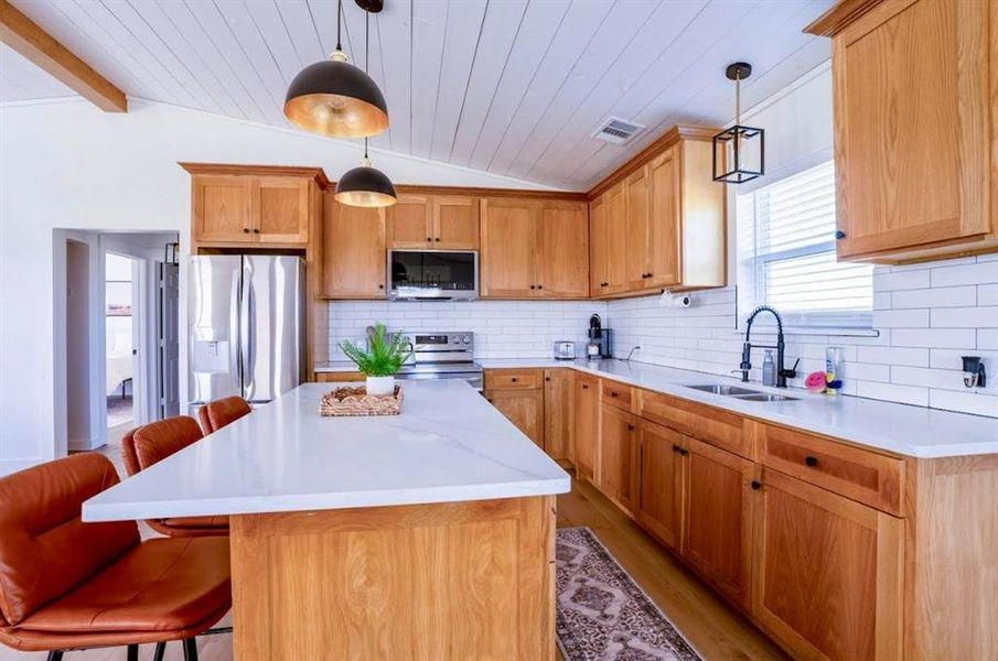 The kitchen features wood cabinetry, white countertops, a white subway tile backsplash, and stainless steel appliances