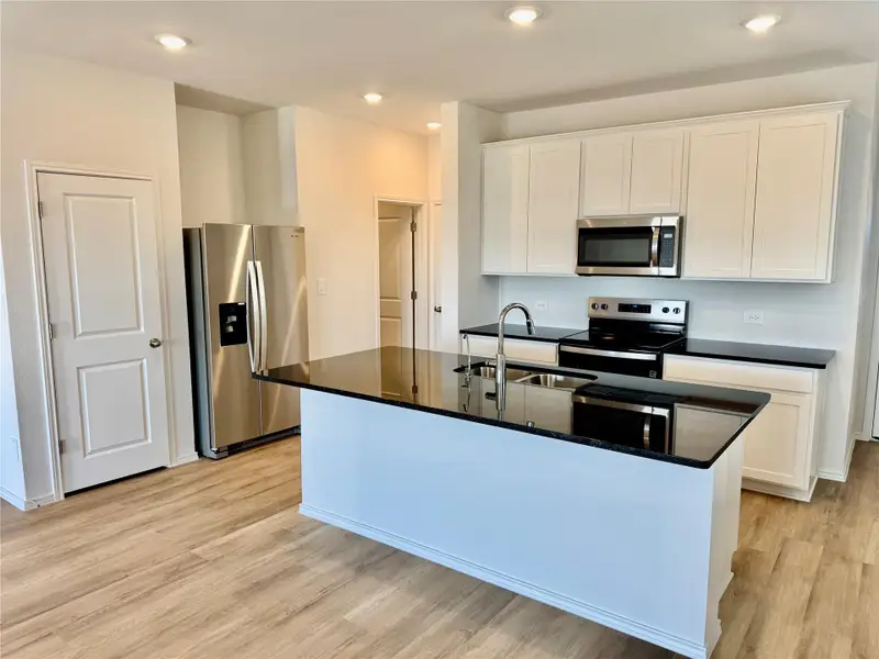 Kitchen with appliances with stainless steel finishes, white cabinets, light wood-type flooring, an island with sink, and recessed lighting