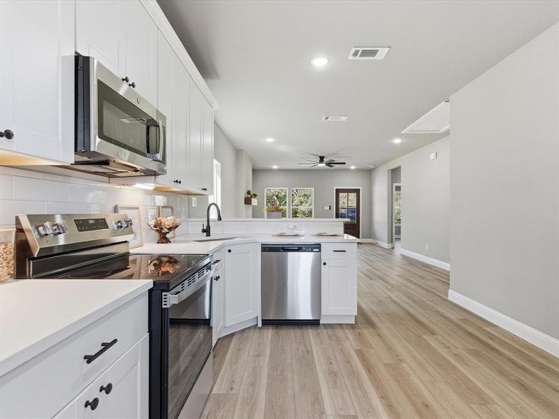 Kitchen featuring stainless steel appliances, recessed lighting, white cabinets, light wood-style floors, and backsplash Kitchen featuring stainless steel appliances, recessed lighting, white cabinets, light wood-style floors, and backsplash