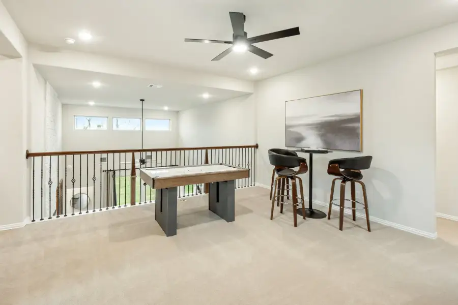 Loft game room with air hockey table, bar-height seating, ceiling fan, and iron railing overlooking lower level
