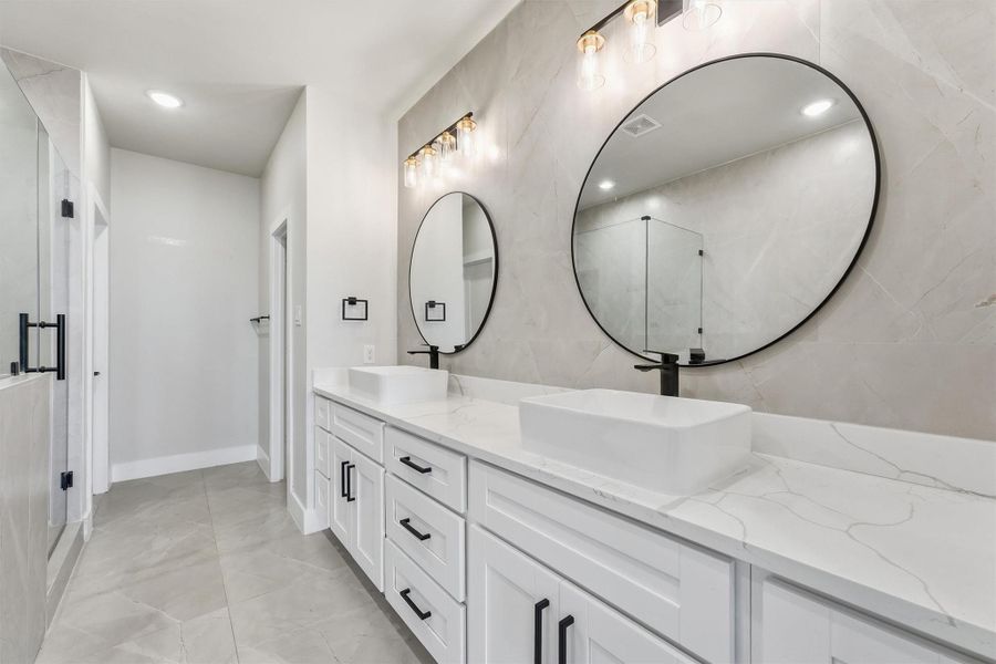 Luxurious primary bathroom featuring dual vessel sinks, quartz countertops, oversized round mirrors, designer lighting, and a spacious walk-in shower with elegant tile finishes.