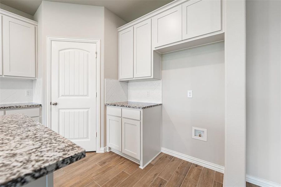 Kitchen with wood finish floors, light stone countertops, white cabinetry, and backsplash Kitchen with wood finish floors, light stone countertops, white cabinetry, and backsplash