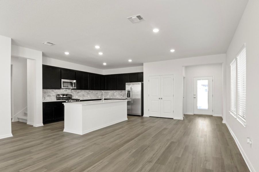 Kitchen with dark cabinets, stainless steel appliances, decorative backsplash, an island with sink, and recessed lighting