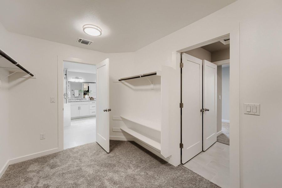 A well-appointed walk-in closet featuring ample shelving and hanging space, connecting to a the primary bathroom and laundry room. A well-appointed walk-in closet featuring ample shelving and hanging space, connecting to a the primary bathroom and laundry room.